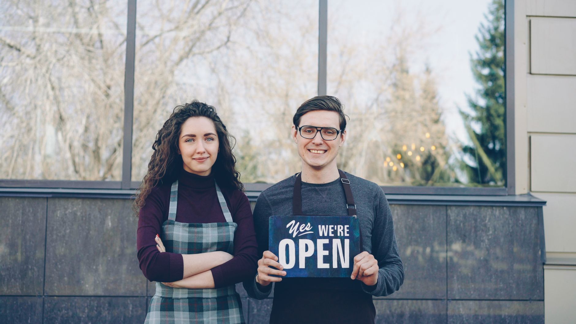 Dos dueños de negocio sonrientes sosteniendo un letrero de abierto frente a su tienda